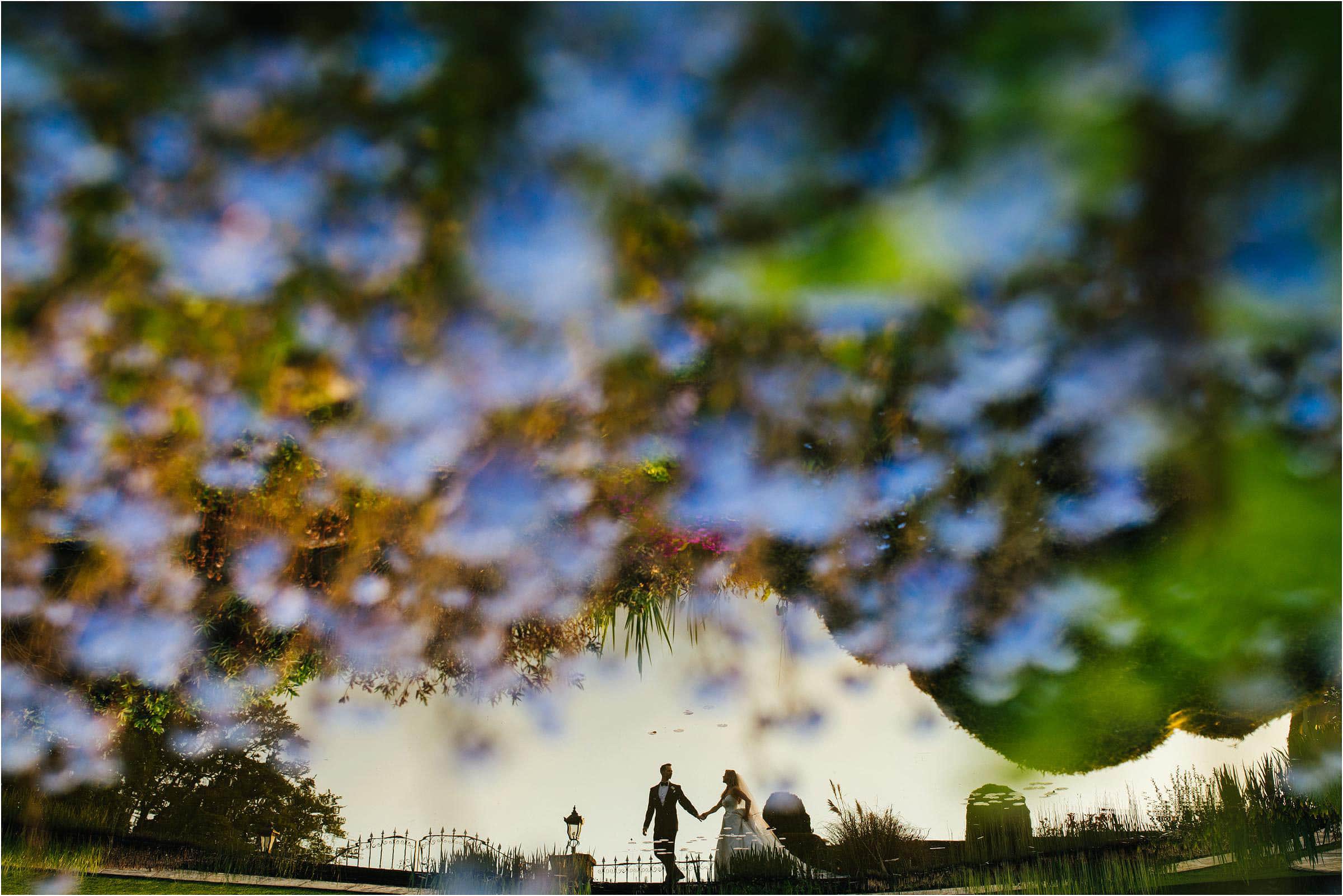 a reflection of a bride and groom in a lake