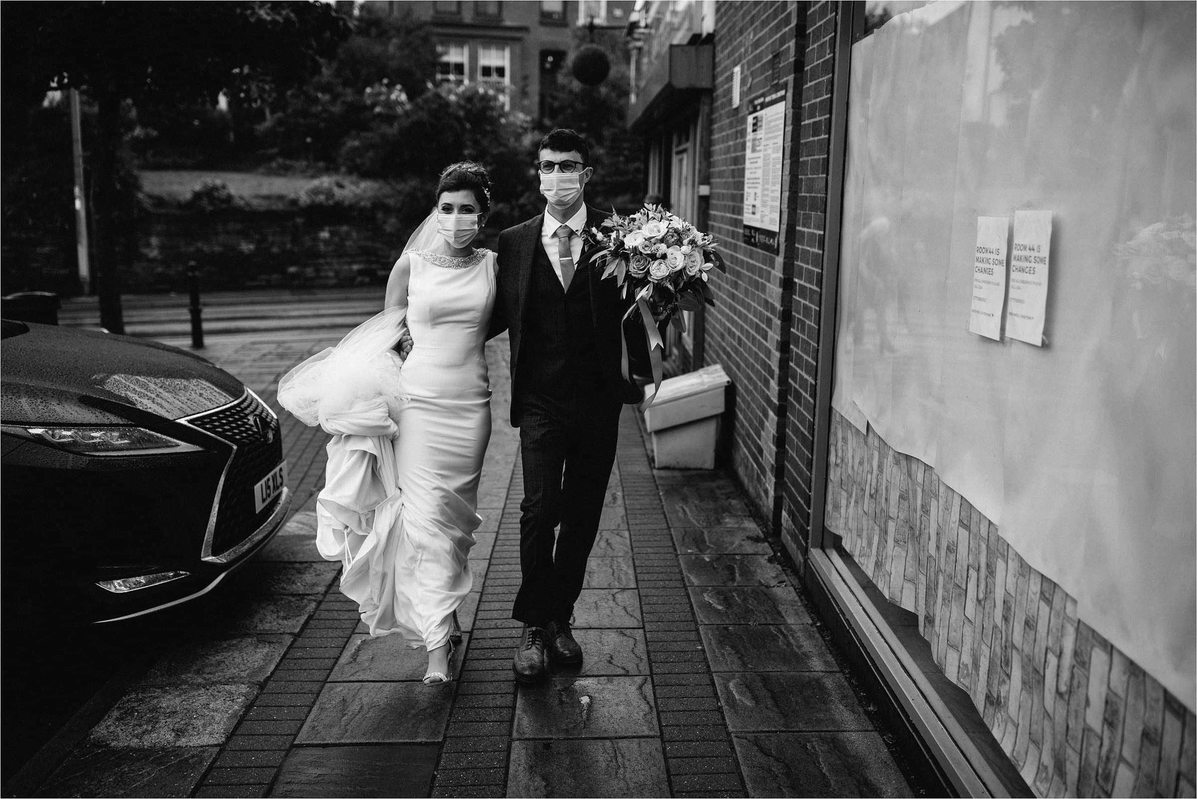 bride and groom walking arm in arm wearing face masks 