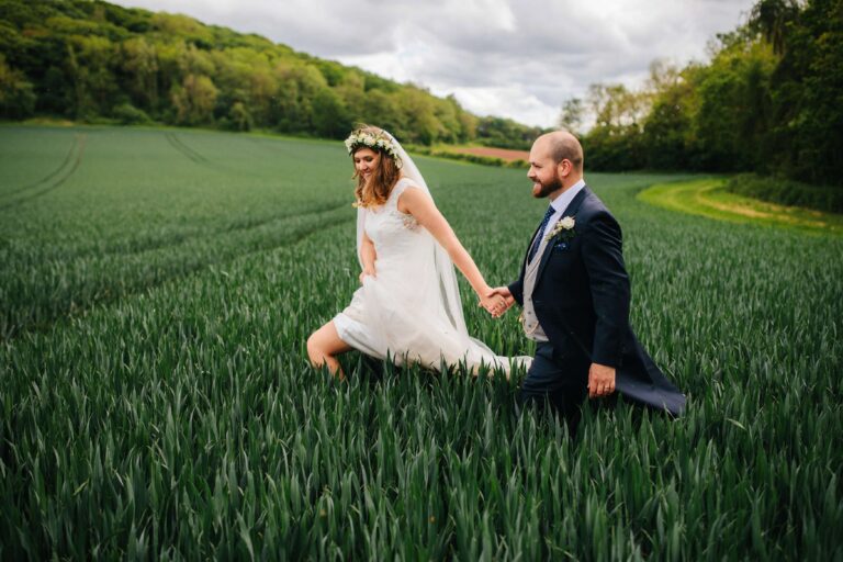 bride and groom walking hand in hand through a field at Brinsop Court